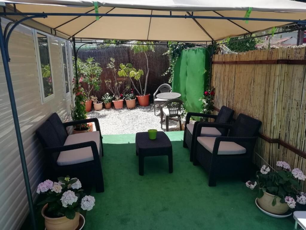 A covered patio with outdoor furniture, potted plants, and a view of a backyard.