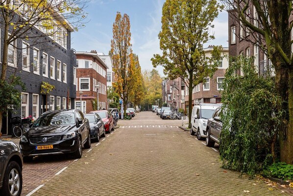 A street lined with parked cars and trees with autumn leaves.
