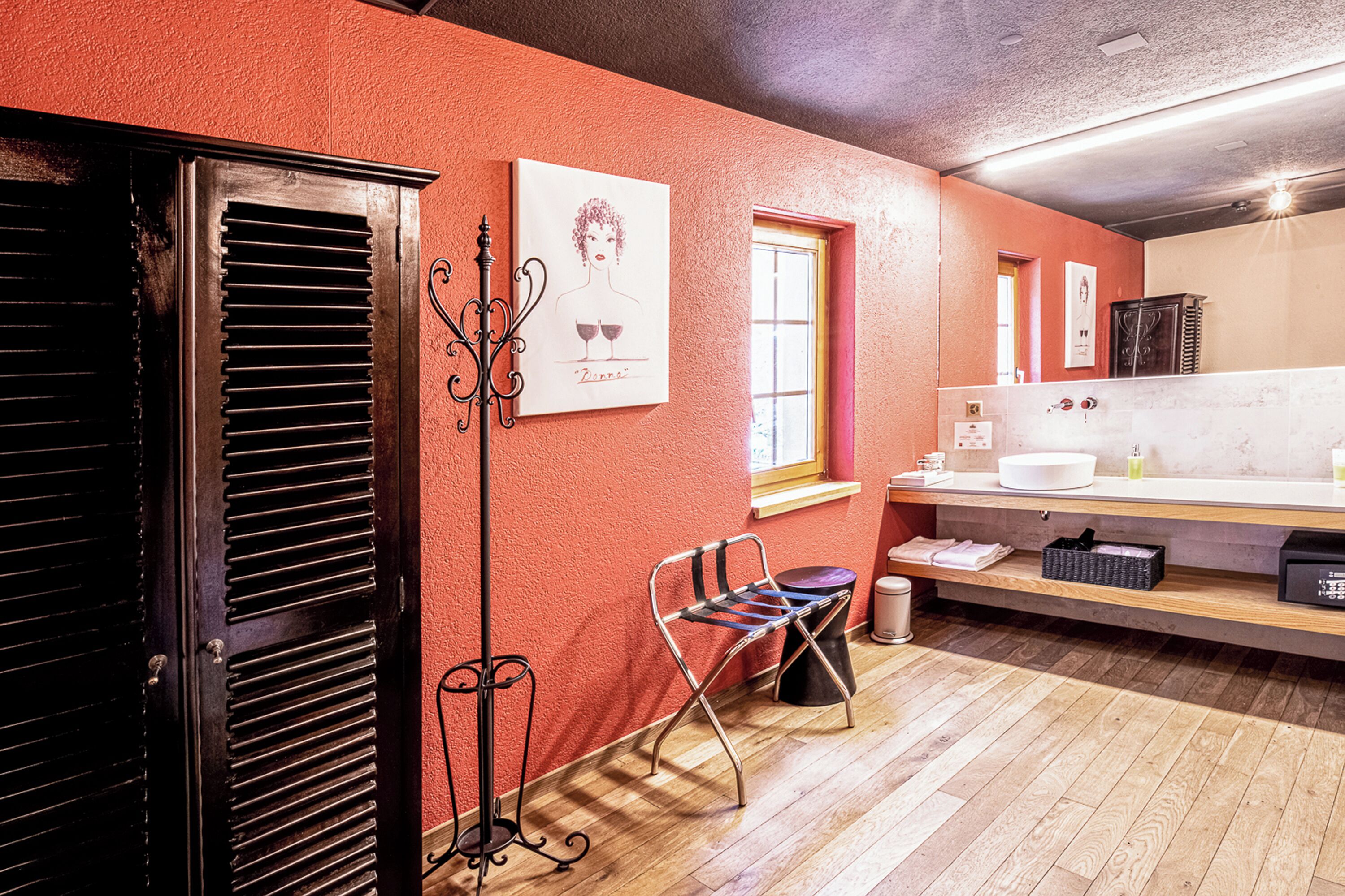 Ein Badezimmer mit Holzboden, Waschbecken, Spiegel, Handtuchhalter und einem Fenster.