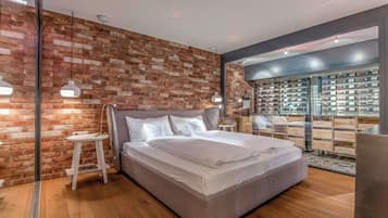 Quarto moderno com parede de tijolos, uma cama grande e um expositor de sapatos ao fundo.