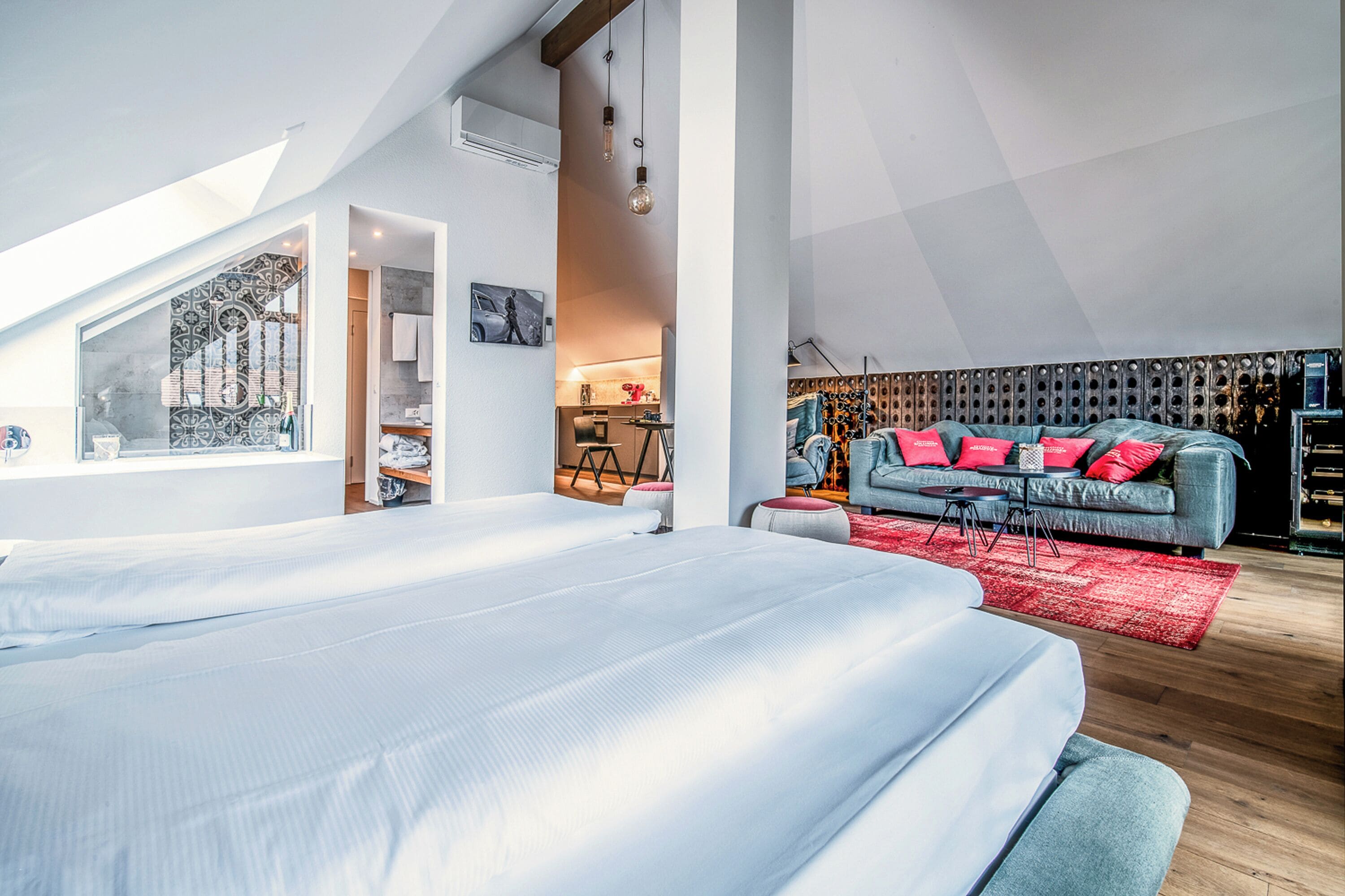 A modern bedroom with a large bed, a red rug, and a grey sofa with red cushions.