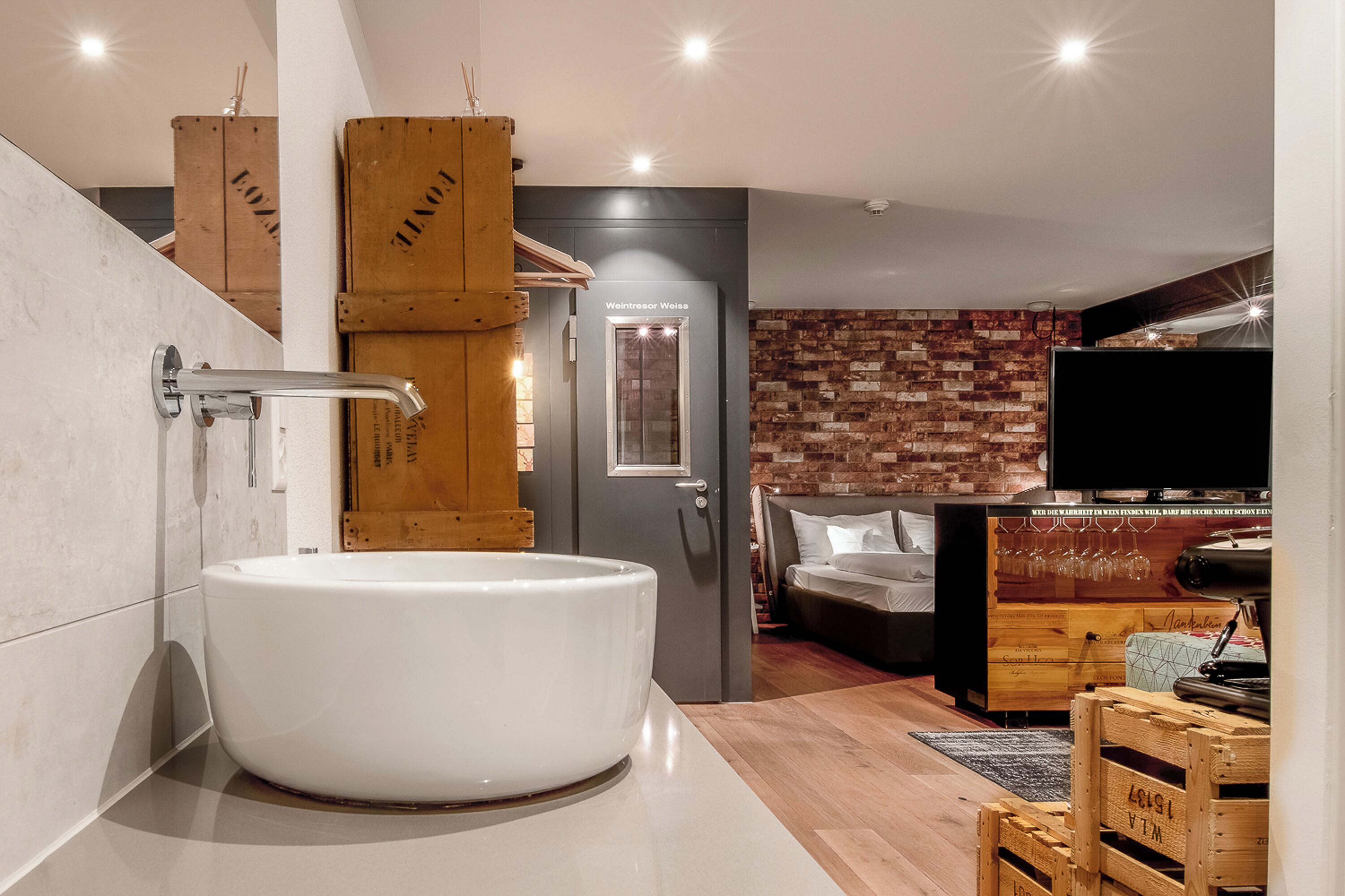 Un baño moderno con una bañera blanca grande, cajas de madera y una pared de ladrillo.