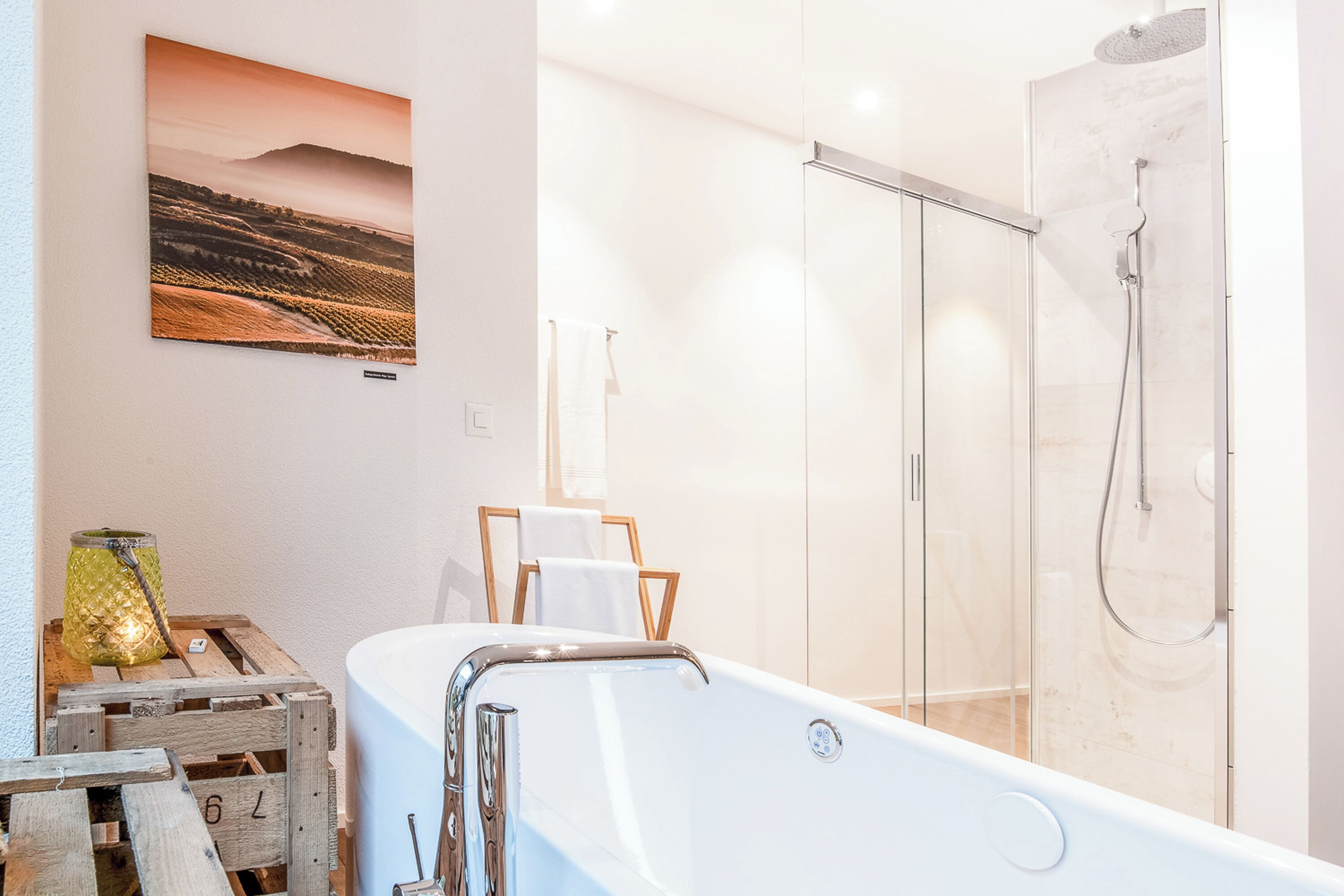 A modern bathroom with a glass-enclosed shower, a white bathtub, and a rustic wooden crate with a lantern.