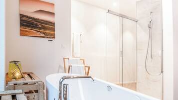 A modern bathroom with a glass-enclosed shower, a white bathtub, and a rustic wooden crate with a lantern.