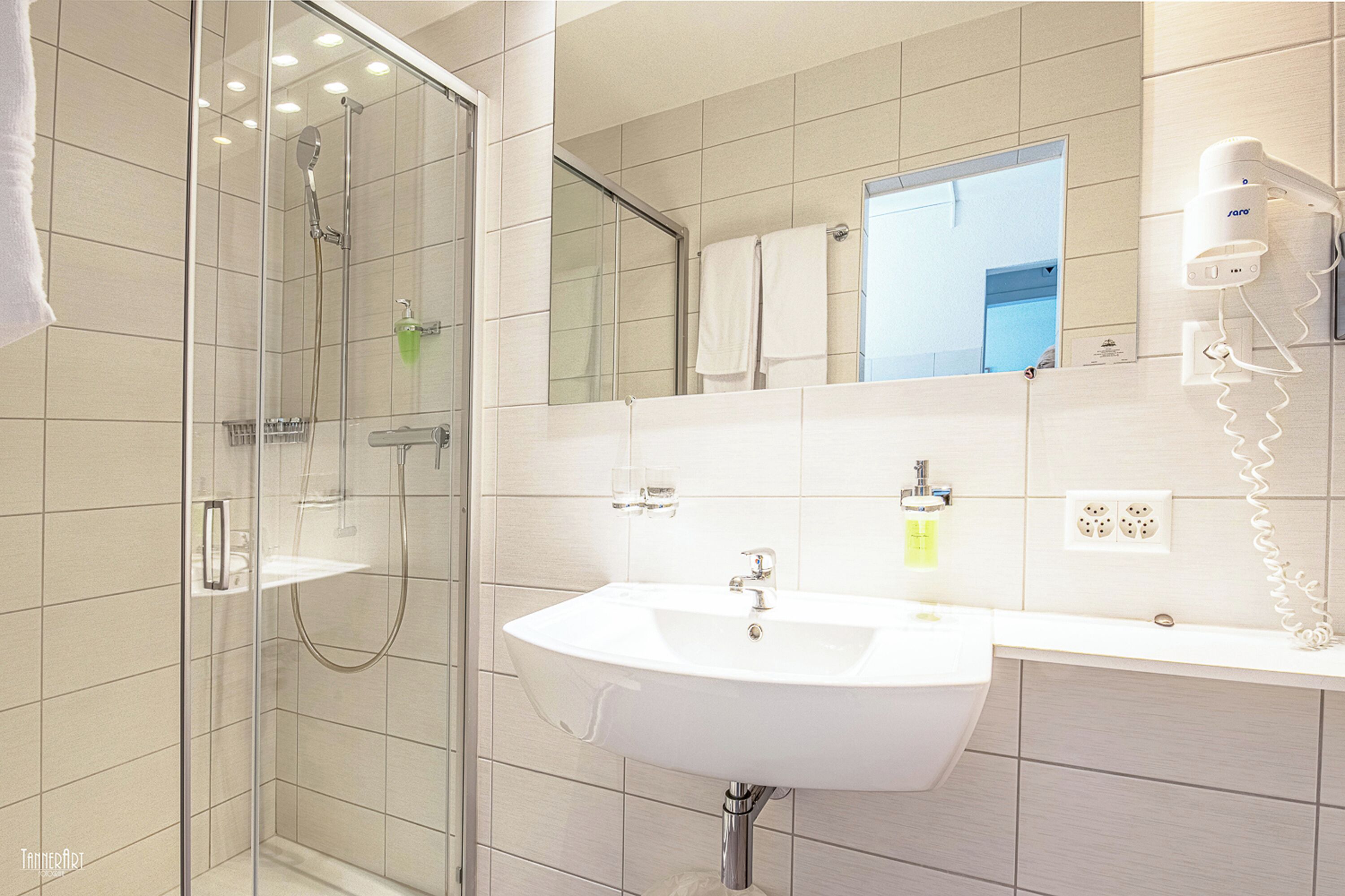 Un baño moderno con ducha de vidrio, lavamanos blanco y espejo sobre el lavamanos.