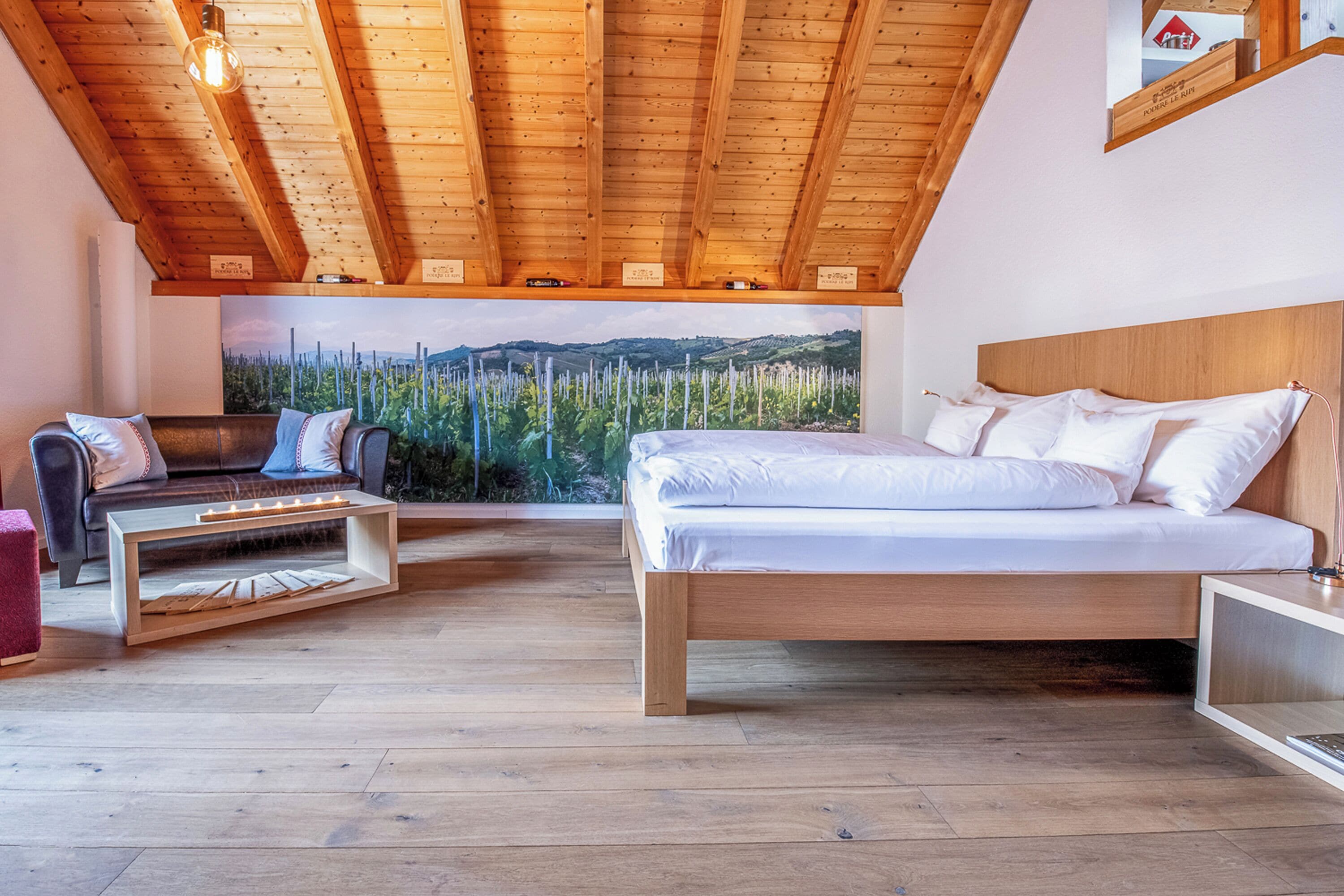 Un dormitorio con techo de madera, cama, sofá y un ventanal con vistas a árboles.