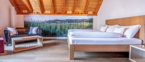 Un dormitorio con techo de madera, cama, sofá y un ventanal con vistas a árboles.