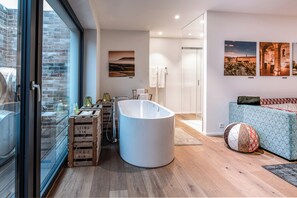 A modern bathroom with a freestanding bathtub, wooden crates, and a cityscape view through a large window. - Hirschen Erlinsbach Swiss Quality (Erlinsbach)