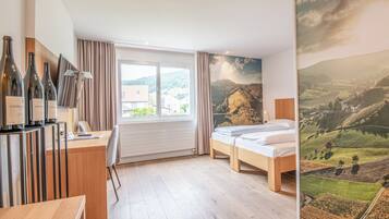 Habitación de hotel con cama, un escritorio con botellas de vino, vistas al campo a través de una ventana y un mural de un paisaje.