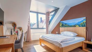 Un dormitorio moderno con una cama de madera, un escritorio y un ventanal con vistas a edificios y montañas.