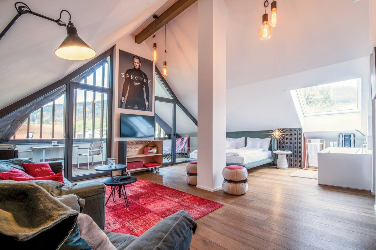 A modern loft bedroom with a large skylight, a cozy seating area, and a view of the outdoors.