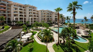 Resort com edifícios de vários andares, área de piscina central e palmeiras.