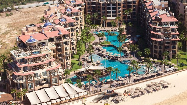 Resort com vários edifícios, área de piscina central e praia.