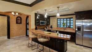 Cozinha com ilha central, banquetas, eletrodomésticos de aço inoxidável e uma grande janela.