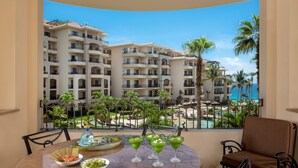 Uma varanda com mesa posta para bebidas e aperitivos, com vista para um resort com vários edifícios e uma piscina.