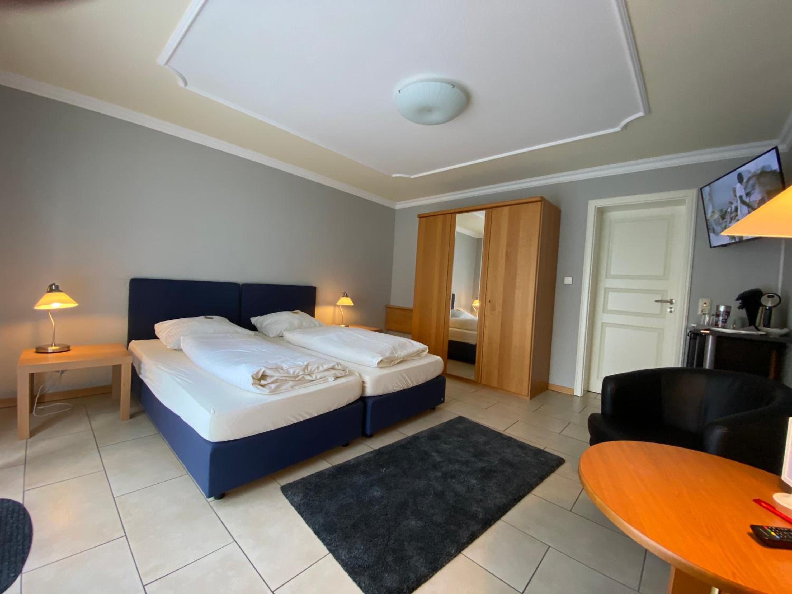 Ein Hotelzimmer mit zwei Betten, einem Schreibtisch, einem Sessel, einem Fernseher und einem Kleiderschrank.