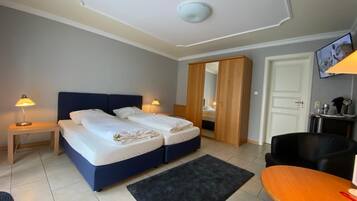 Ein Hotelzimmer mit zwei Betten, einem Schreibtisch, einem Sessel, einem Fernseher und einem Kleiderschrank.