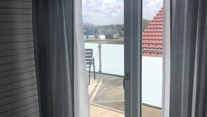 Une pièce dotée d’une porte-fenêtre coulissante qui donne sur un balcon offrant une vue sur un bâtiment au toit rouge et un ciel dégagé.