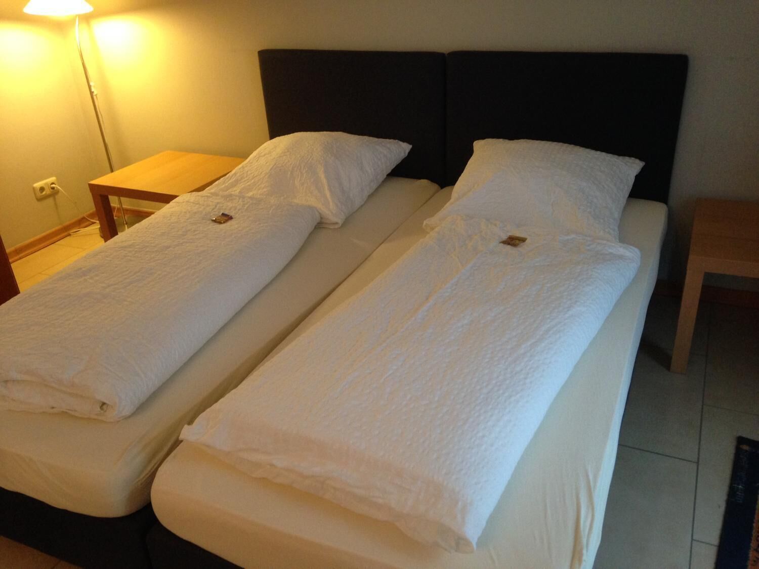 A double bed with a dark headboard and white linens, two bedside tables, and a lamp on the left.