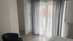 Une chambre à coucher avec un lit, une chaise et une vue sur l’extérieur à travers de fines rideaux.