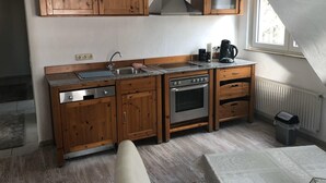 Une cuisine de taille réduite, dotée de meubles en bois, d’une cuisinière à gaz, d’un four et d’une fenêtre laissant entrer la lumière naturelle.