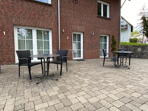 A brick building with numbered windows and a paved patio area with outdoor furniture. - Gästehaus Savo (Nuerburg)
