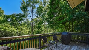 Une terrasse en bois, aménagée avec du mobilier d’extérieur, notamment une table ronde et deux chaises, donnant sur une zone boisée.