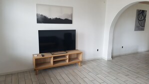 Una sala de estar con un televisor de pantalla plana sobre un soporte de madera, un cuadro de paisaje en la pared superior y un reloj.