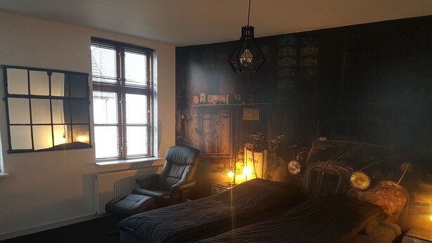 Un dormitorio con una cama, una silla, un radiador, una ventana y una pared con diversos objetos.