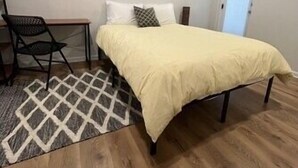 Une chambre à coucher avec un lit, une chaise, un tapis et un tableau accroché au mur.