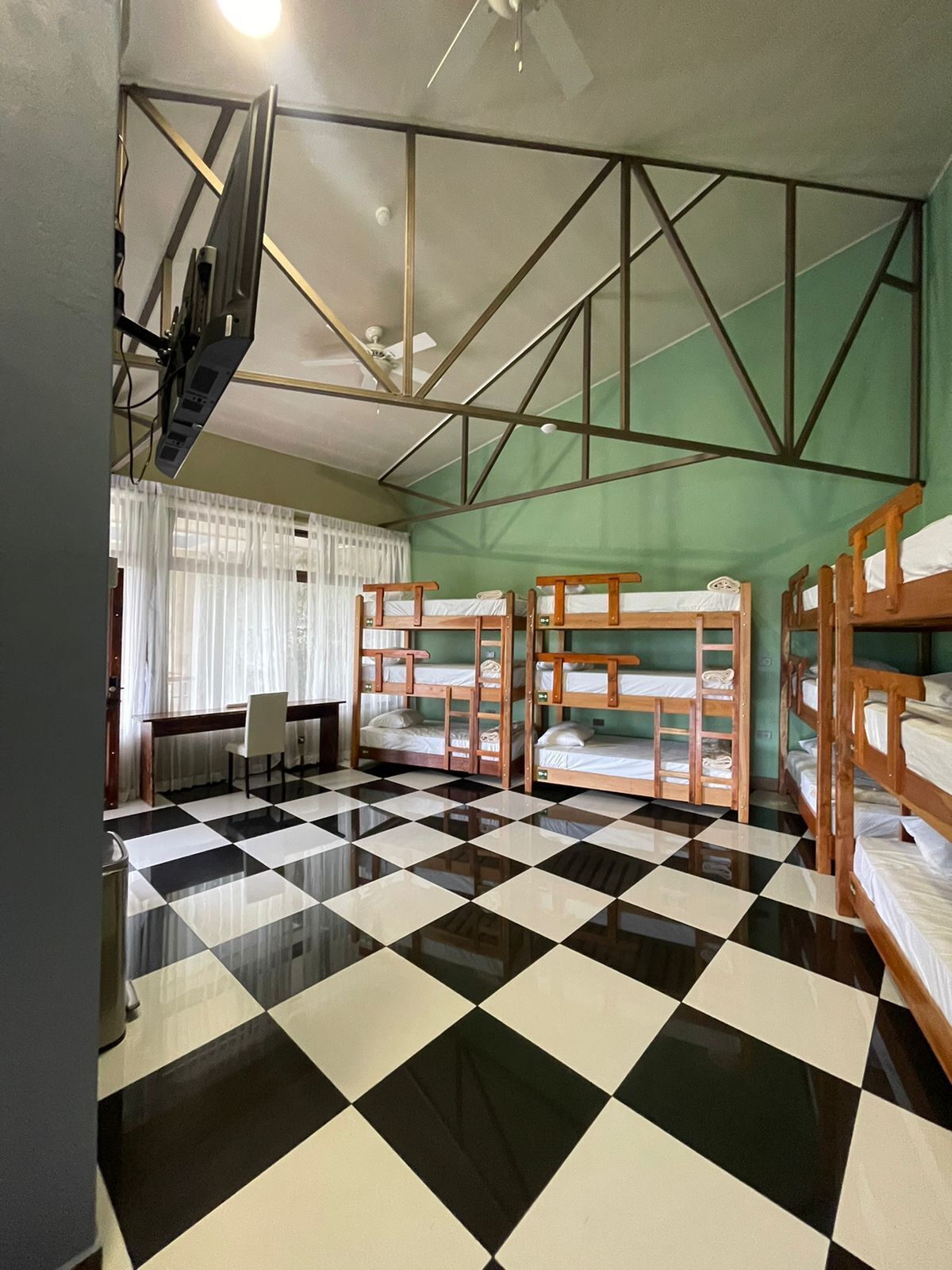 Un dormitorio con literas, piso a cuadros, un escritorio con silla y una ventana con cortinas.