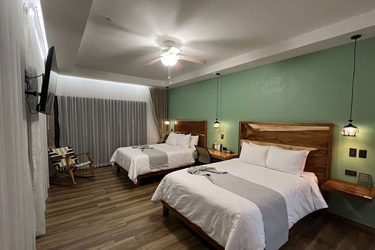 A hotel room with two beds, a ceiling fan, a TV mounted on the wall, and a wooden floor.