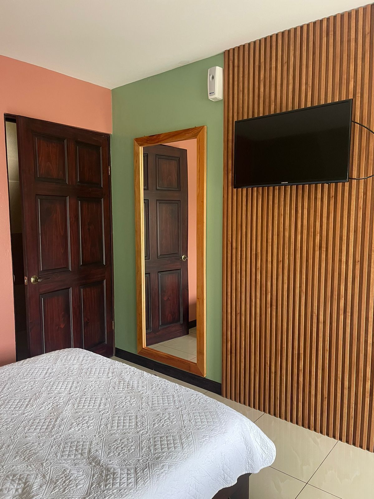 A bedroom with a bed, a wooden slat wall, a door, and a mounted television.