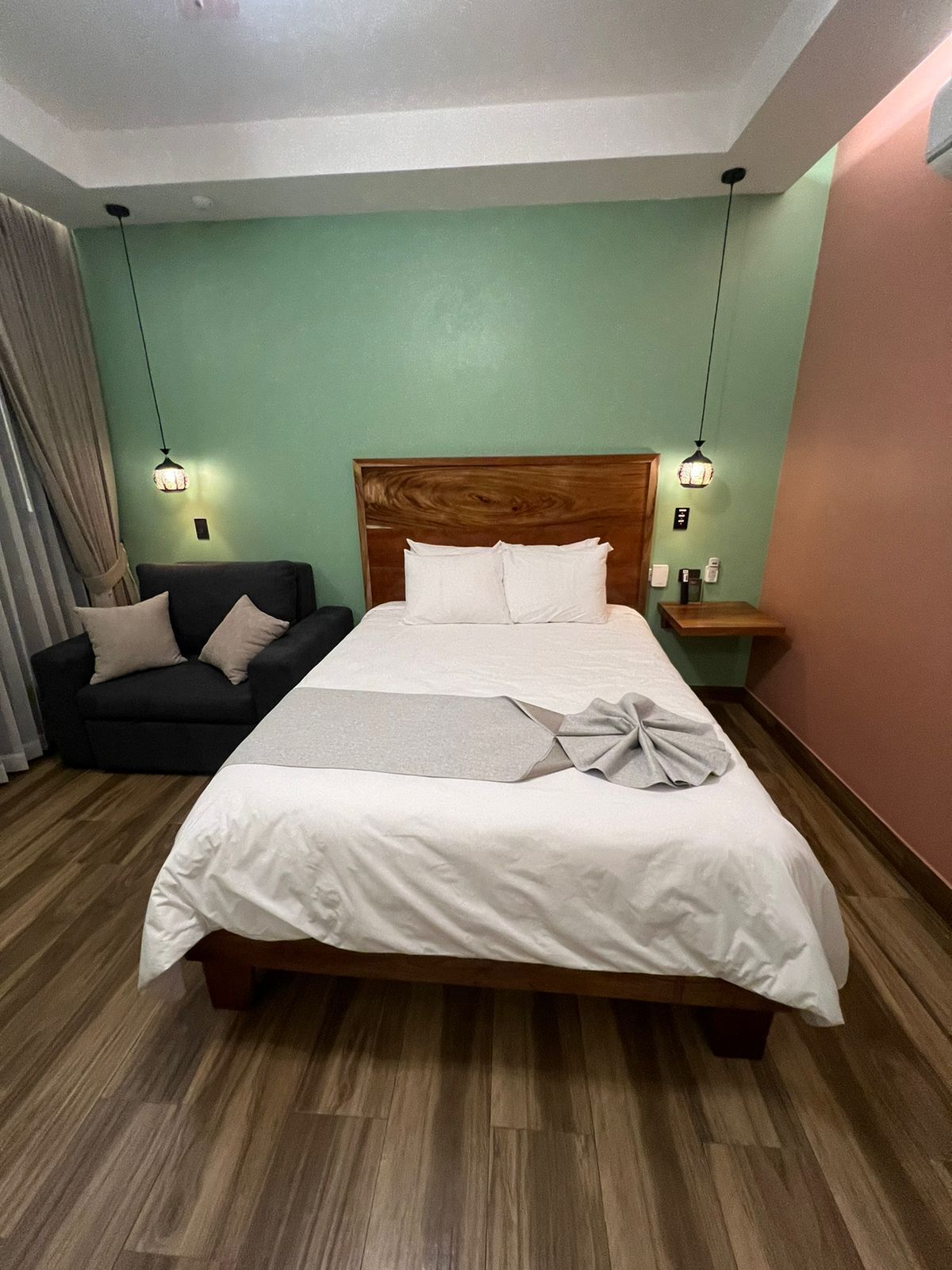 Habitación de hotel ordenada con una cama grande, un sofá, una mesita de noche y una lámpara.