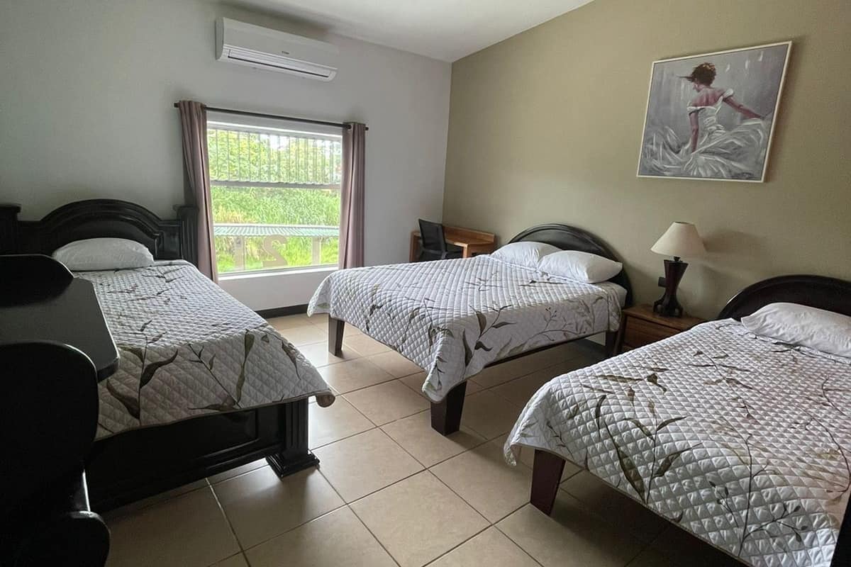 A hotel room with two beds, a desk, a chair, a window with curtains, and a painting on the wall.