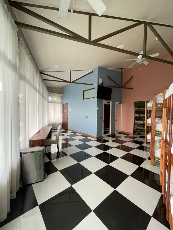 A hotel room with a checkered floor, a desk, a chair, a bed, and a ceiling fan.