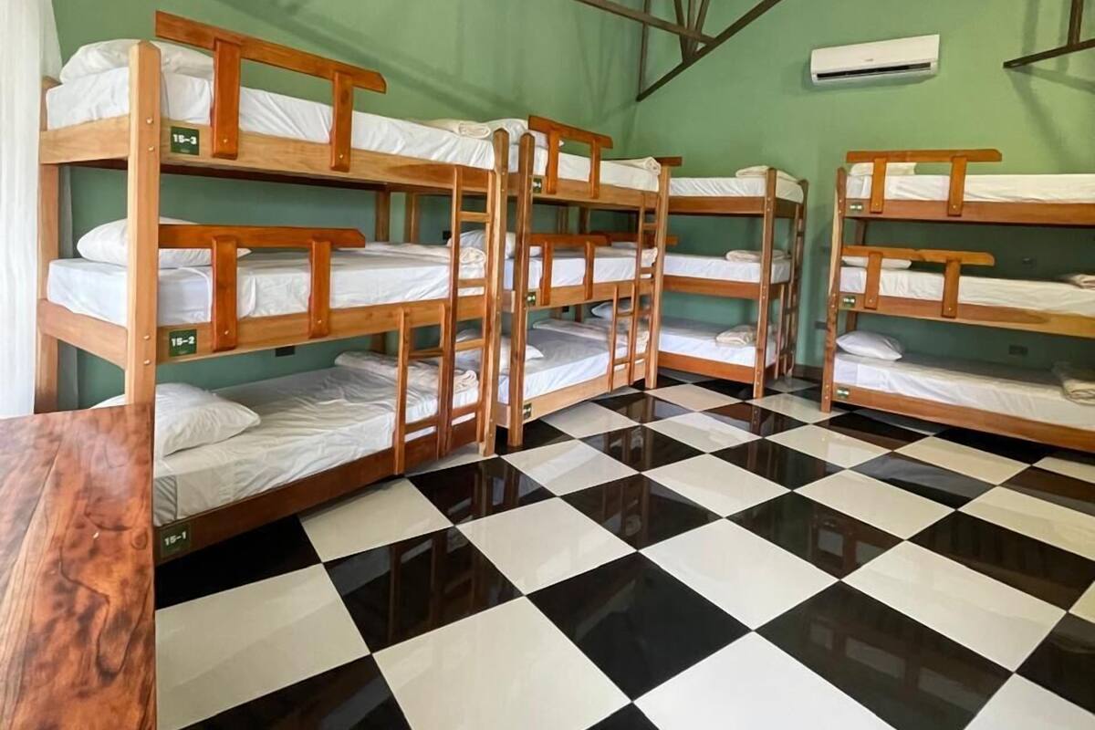 A dormitory room with bunk beds, a checkered floor, and a ceiling fan.