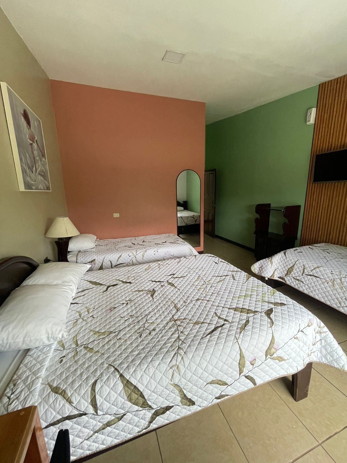 Una habitación de hotel con dos camas, un espejo, una lámpara y un cuadro en la pared.