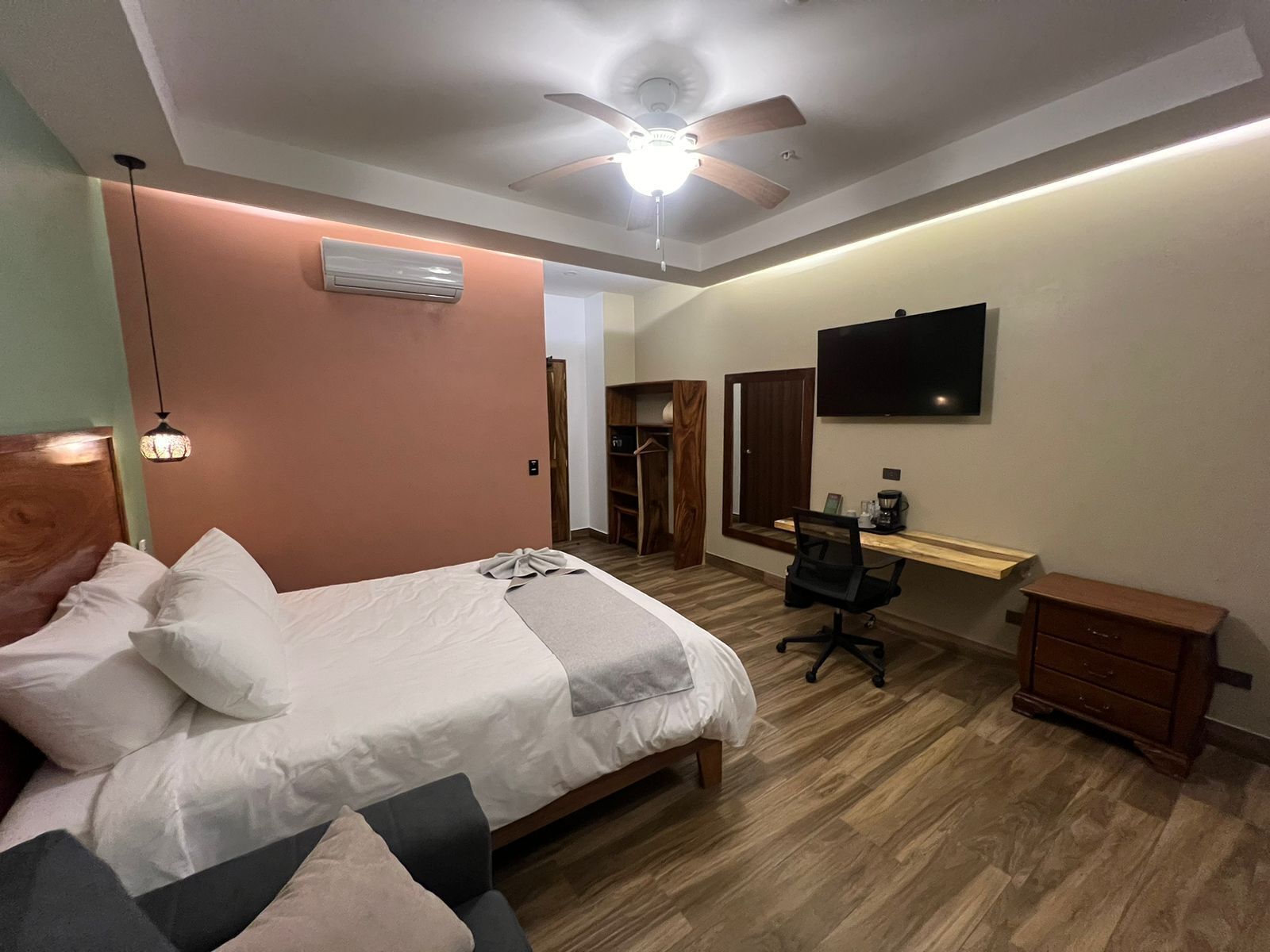 A bedroom with a bed, a desk, a chair, a TV, and an air conditioner.