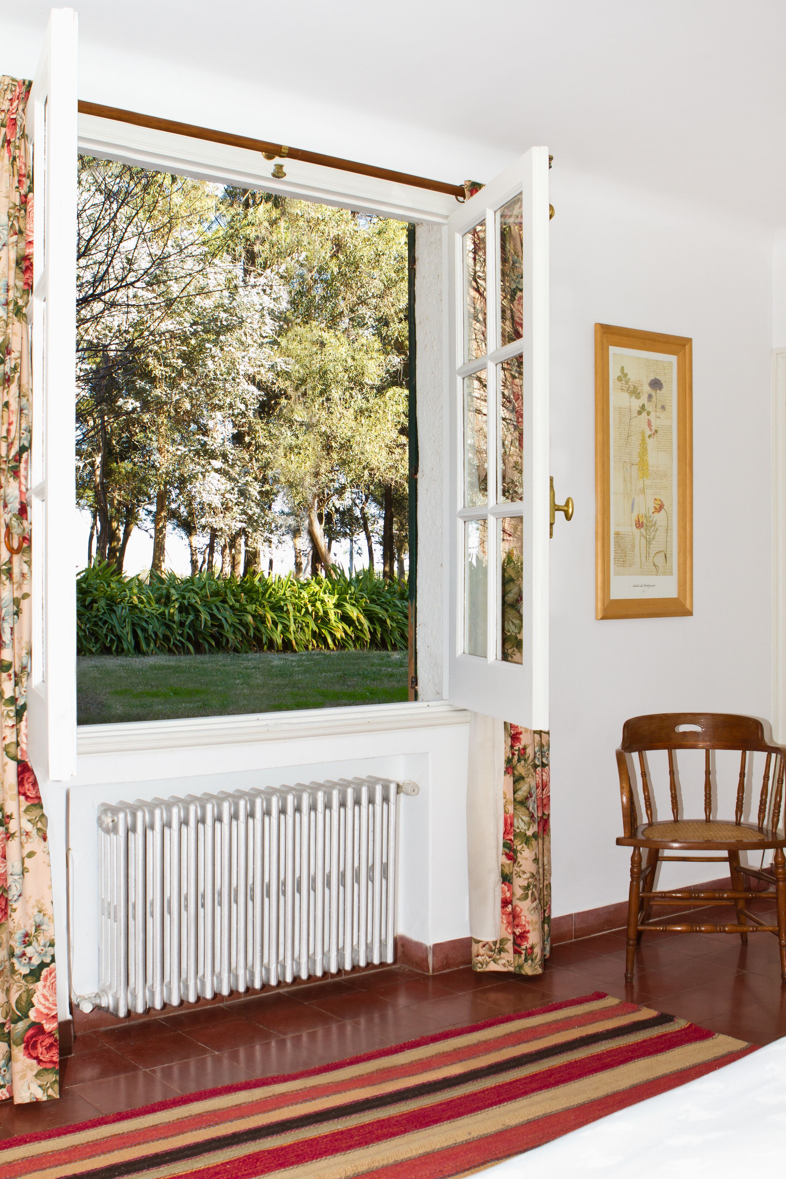 A room with a large window, a radiator, a chair, and a framed picture on the wall.