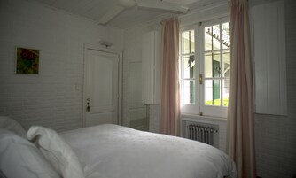 Un dormitorio con cama, una puerta blanca, una ventana con cortinas y un radiador.