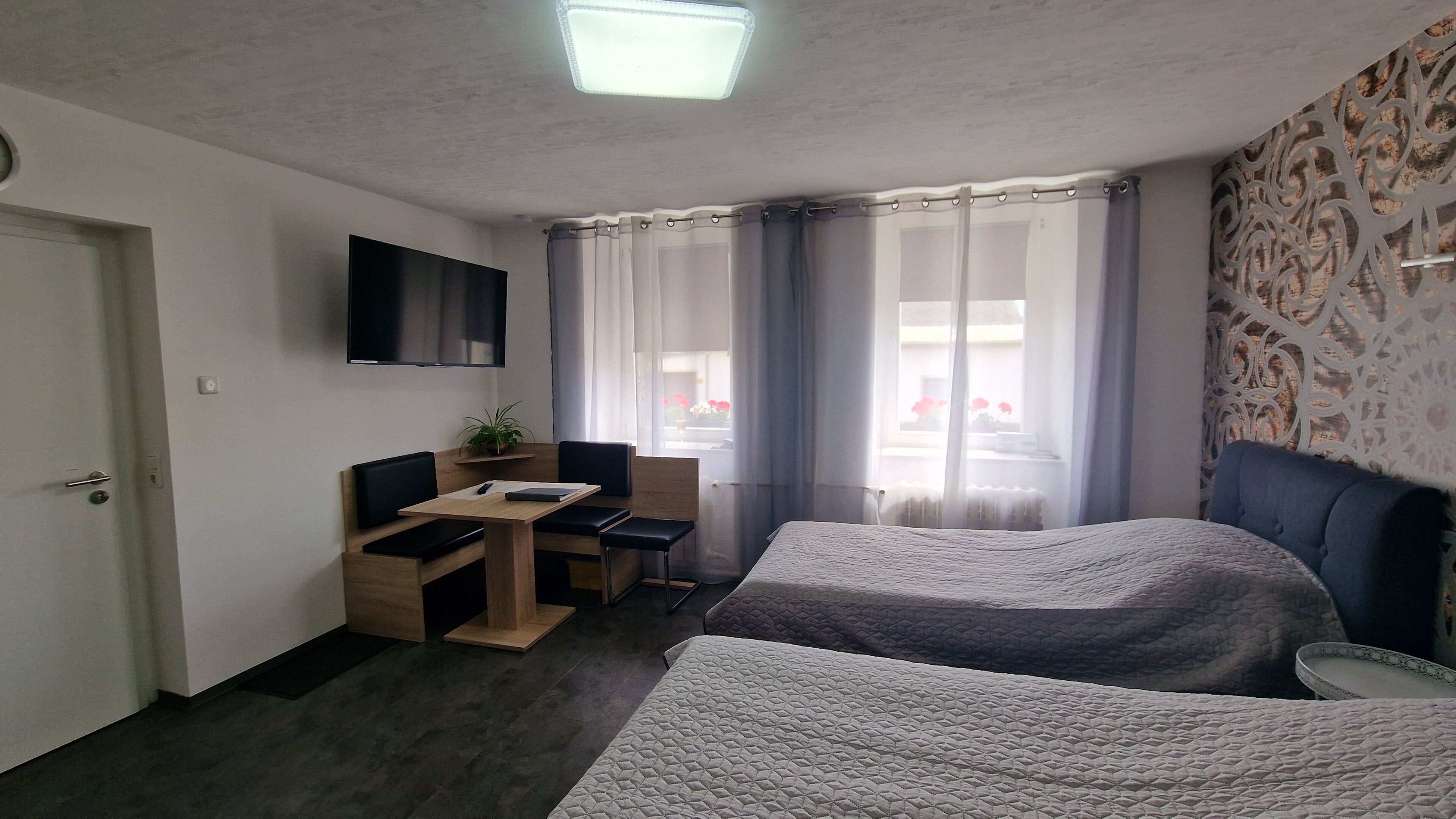 A hotel room with two beds, a desk with a chair, a TV mounted on the wall, and a window with curtains.