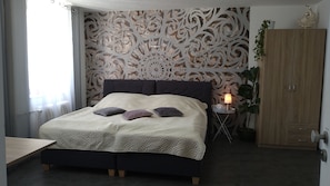 Un dormitorio con una cama grande, una mesita de noche con lámpara, un armario y un panel decorativo en la pared.