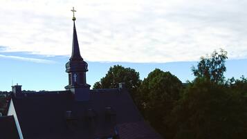 Een kerktoren met een kruis bovenop, omringd door bomen en een heldere lucht.