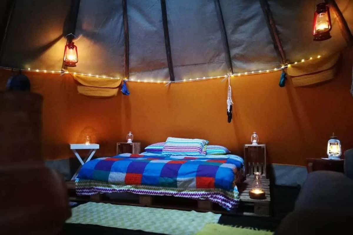 Um quarto em tenda aconchegante, com uma cama, duas mesas de cabeceira e luzes de cordão.