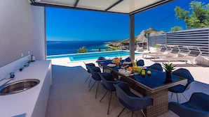 A modern outdoor dining area with a view of the sea and a pool.