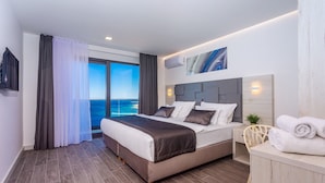 A modern hotel room with a large bed, a desk, and a view of the sea.