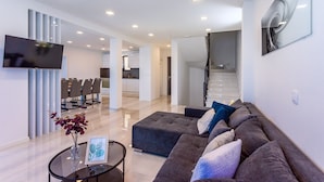 A modern living room with a sectional sofa, a flat-screen TV, and a dining area with chairs and a table.