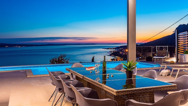 A poolside area with a glass table, chairs, and a bottle of wine.