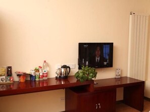 A room with a wooden desk, a television mounted on the wall, and various items on the desk including a plant, a kettle, and some containers. - GreenTree Alliance Zhangjiakou Jingkai Weisan Rd (Zhangjiakou)